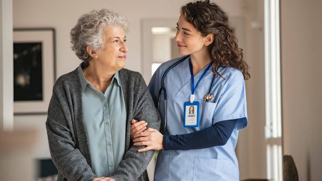 older woman being guided by the arm by a younger female nurse