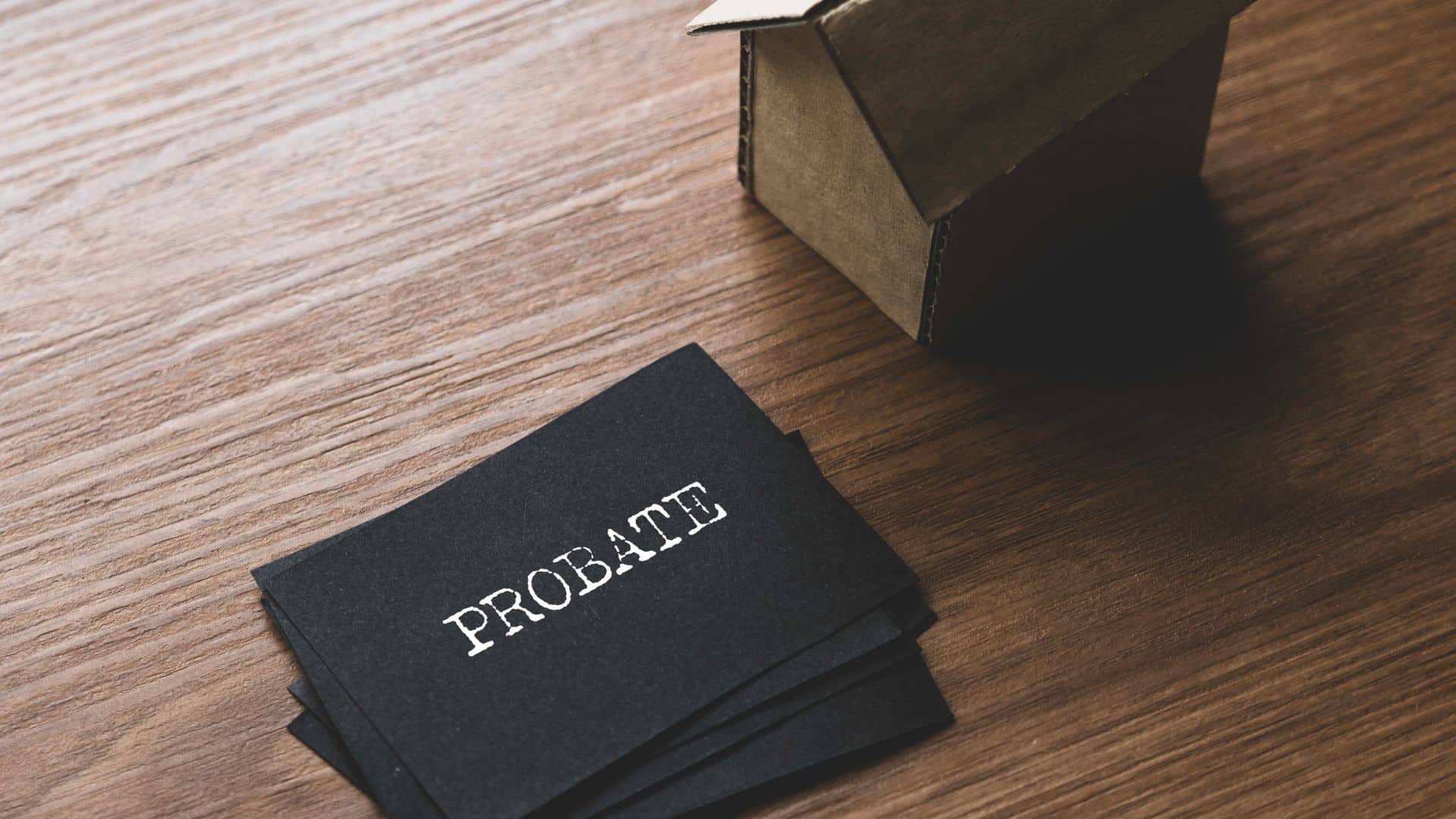 black card that reads "PROBATE" on a desk next to a small wooden house figure