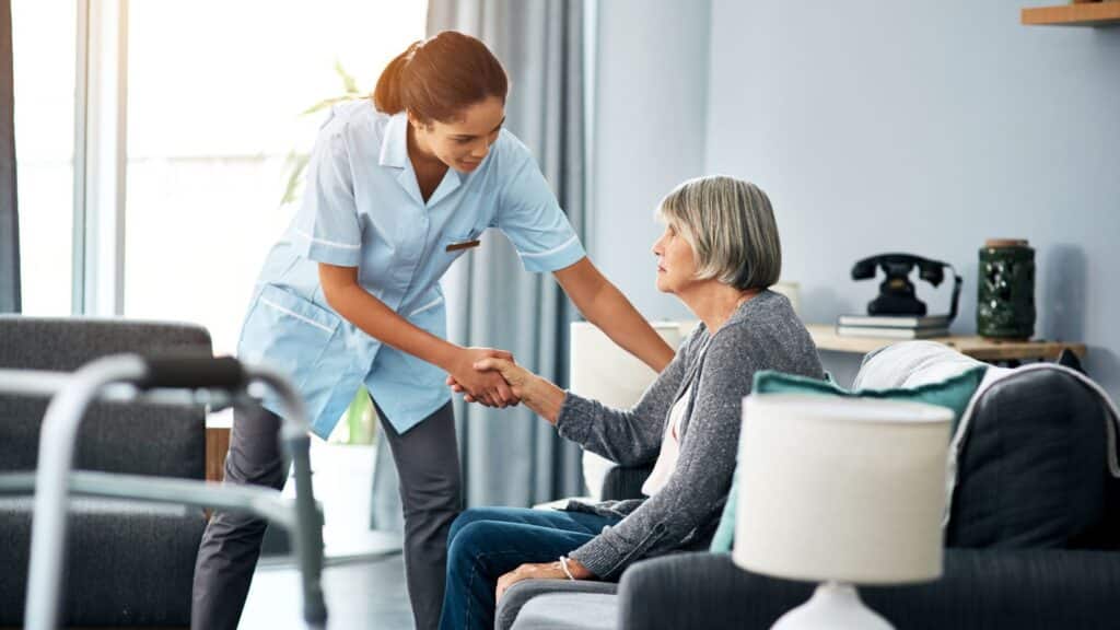 older woman sitting on a couch while a home healthcare nurse assists her