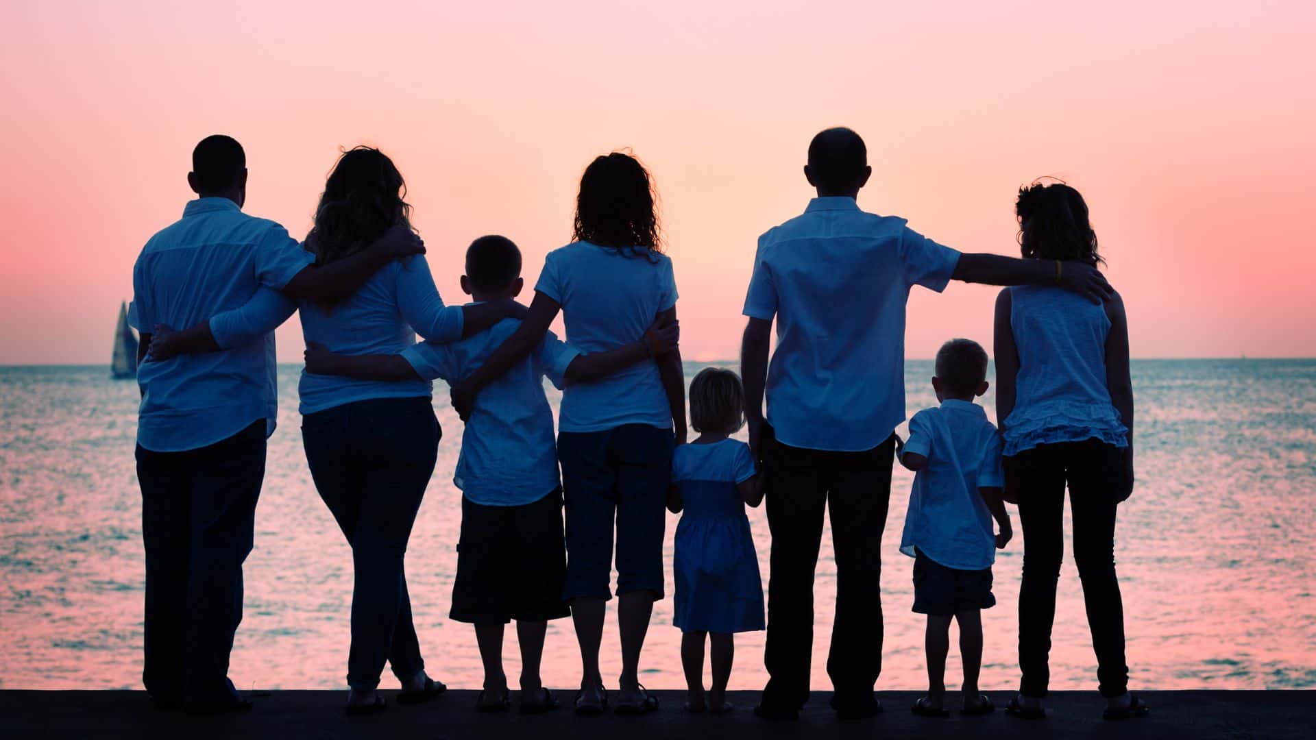 family standing on the shore, silhouetted against the sunset