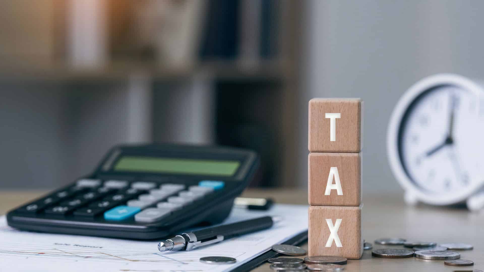 blocks spelling out TAX on a desk next to a calculator and clock