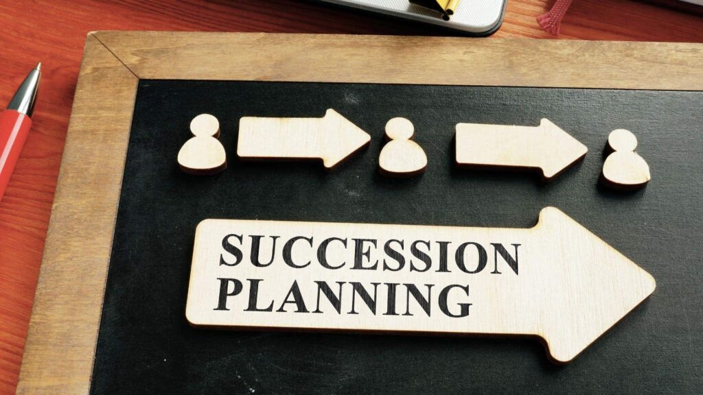 Wood cutouts on a chalkboard. One large arrow reads "succession planning" beneath three people shapes separated by arrows