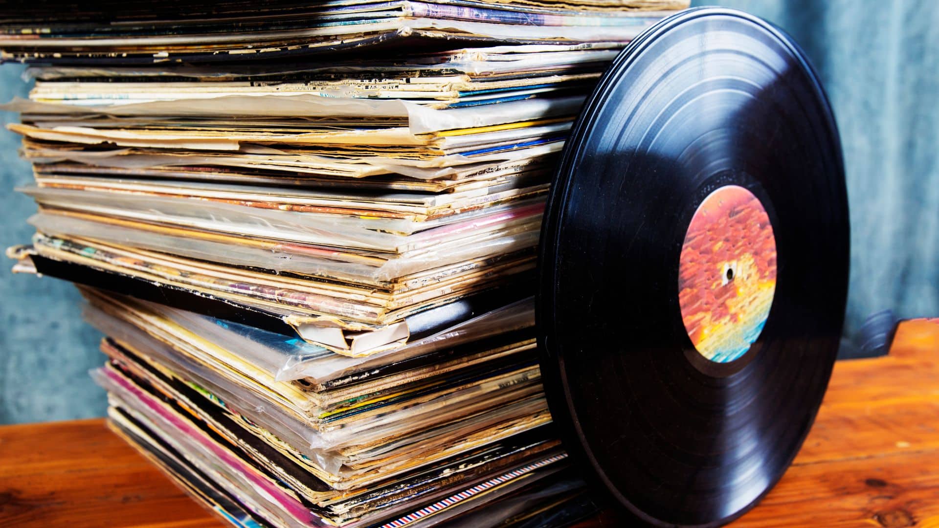 A stack of vinyl record sleeves with a single record standing upright next to them.